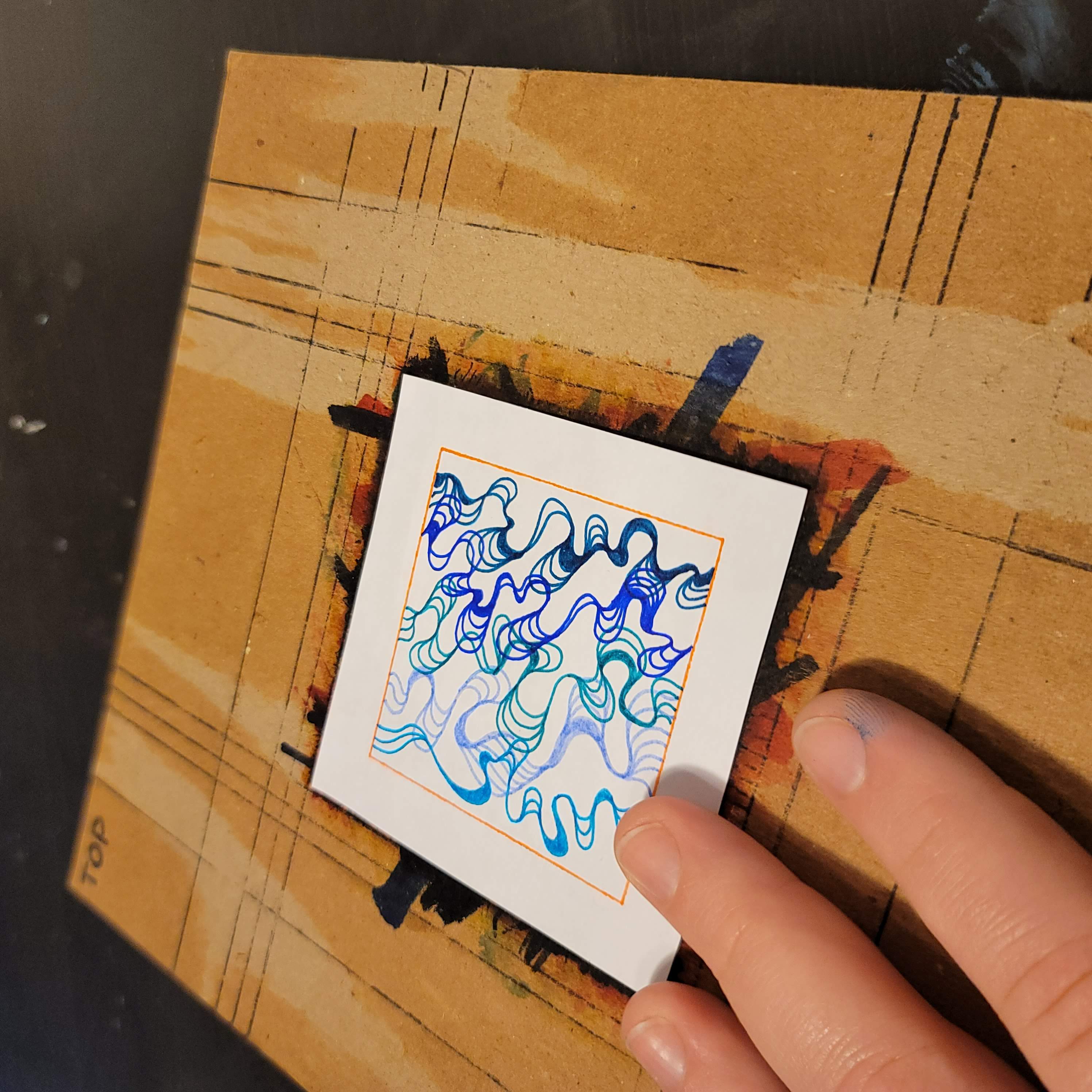 An artist creating a blue-toned wiggling line artwork atop an art board
