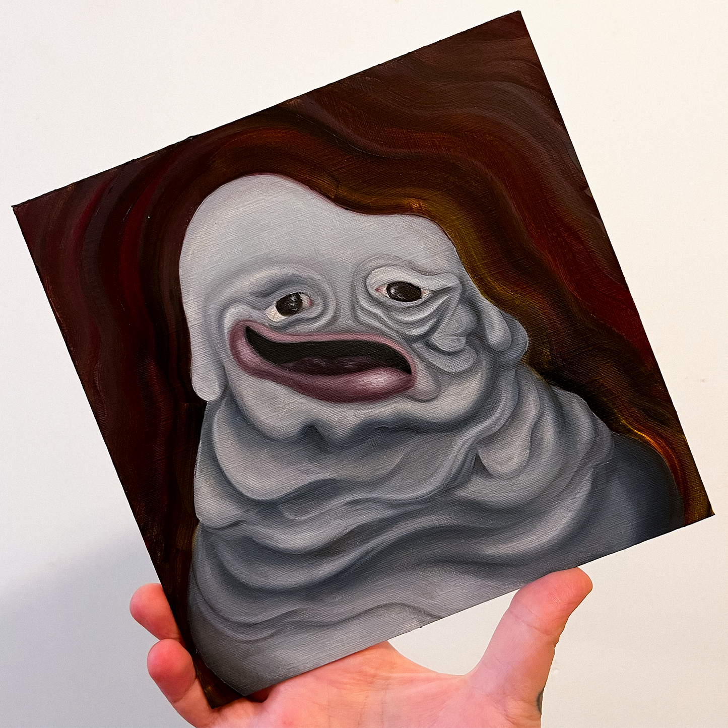 A hand holding a painting of a grey mass in a heavy dripping pile with a face that appears to be slowly sinking